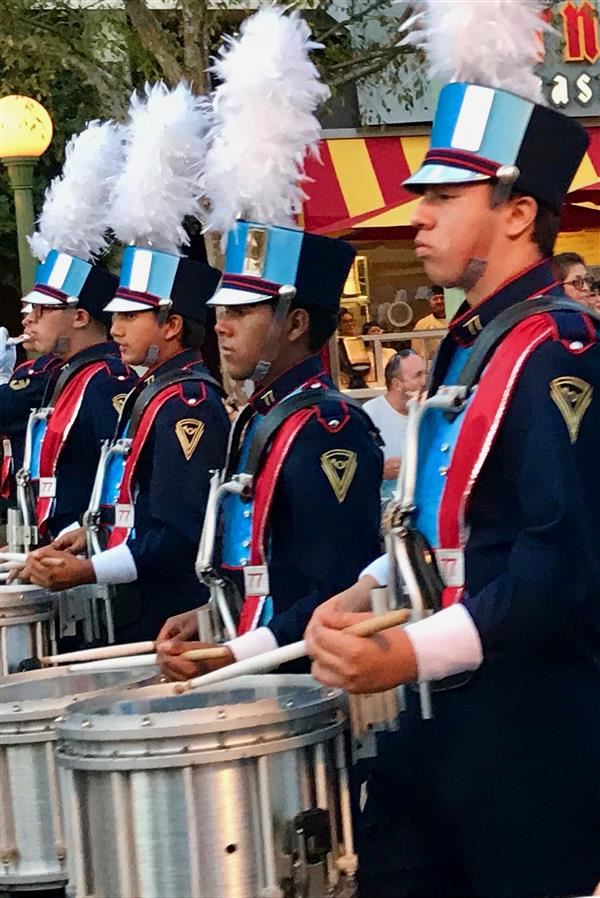 Close up of four male high school band members marching down a street, all in plumed hats. Close up of four male high school band members marching down a street, all in plumed hats.